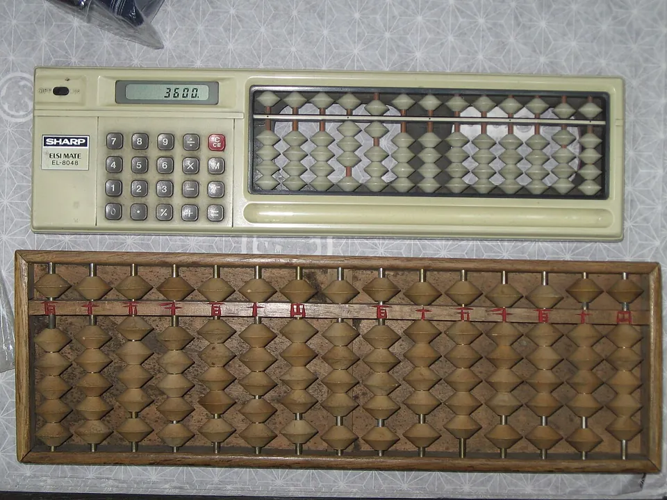 A wooden abacus beside a Sharp electronic calculator on a patterned tablecloth.